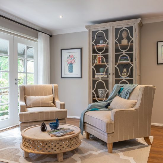 Sitting room, Hamptons style, armchairs, timber coffee table, throw blanket, Hamptons cabinet, bookcase, glass panelled bookcase, floor rug, French doors, white curtains, sheer curtains, iron curtain rod, wall art